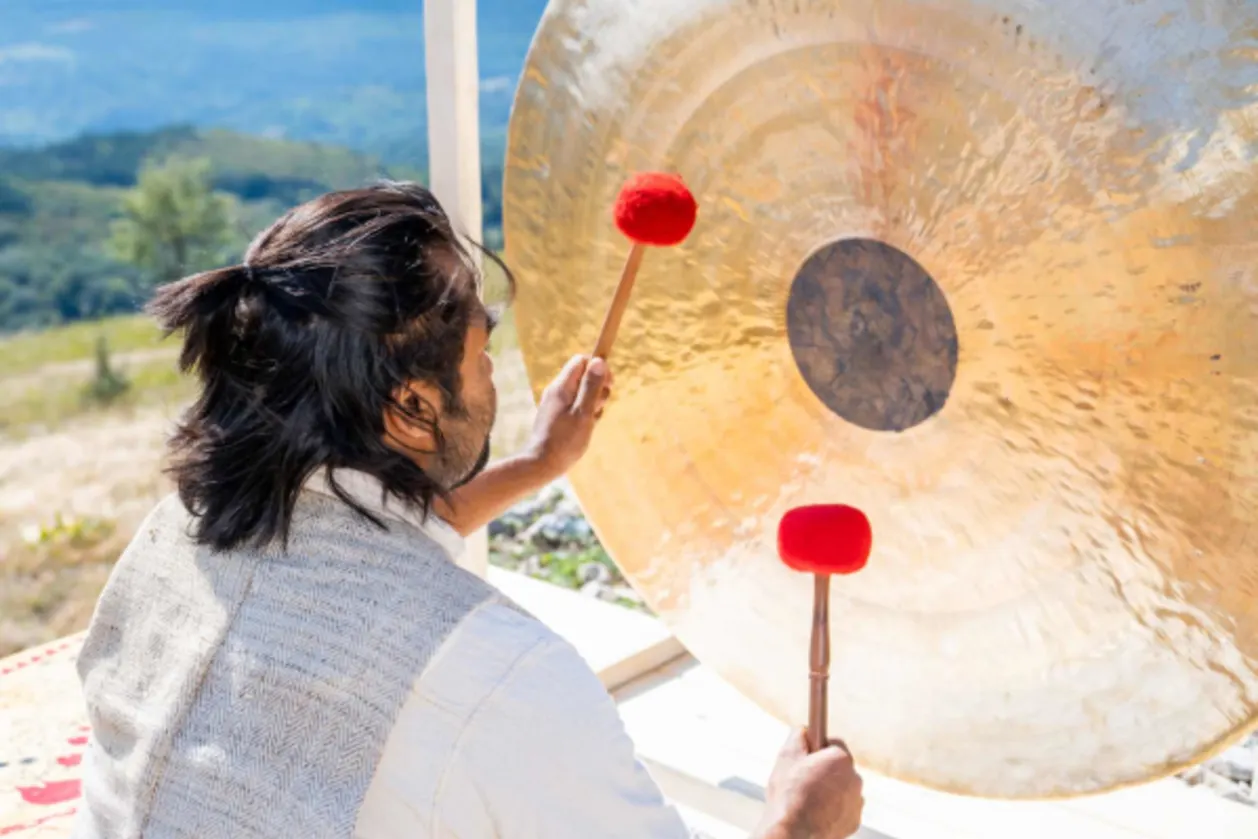 man playing bronze gong on sound healing retreat